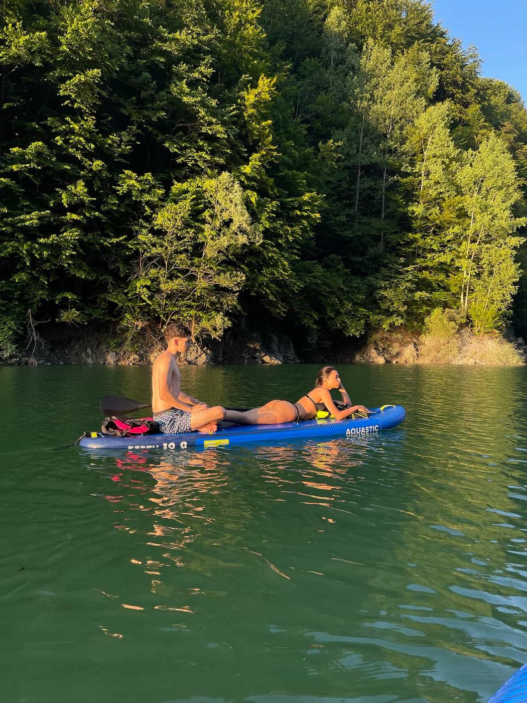 Doi tineri relaxându-se pe o placă SUP în lumina serii, pe Lacul Paltinu